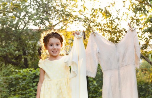 Cute little girl in dress washing white clothes in metal basin in backyard, child helping with
