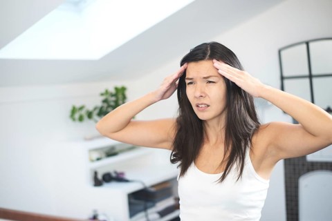 Attractive young woman with a migraine headache standing holding her fingers to her temples with