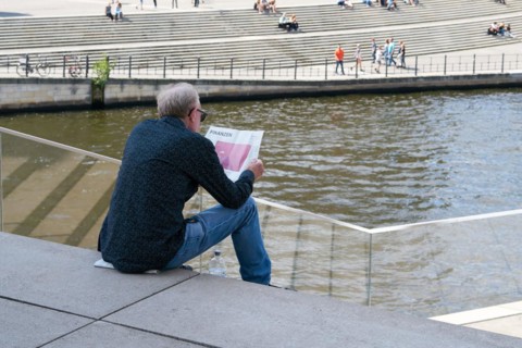 A man sits on a step in the government district of Berlin and reads the financial section of a
