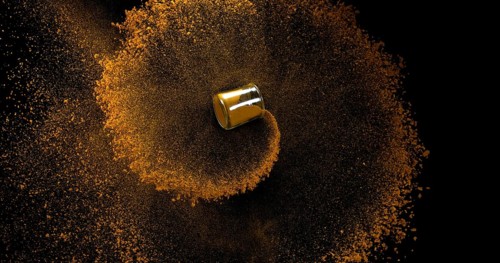 Curry Powder into a Small Jar falling against Black Background