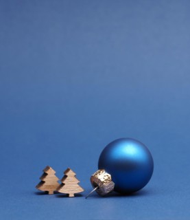 Blue Christmas tree ball with small wooden tree shapes on a blue paper background with space for