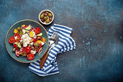 Greek fresh healthy colorful salad with feta cheese, vegetables, olives in blue ceramic bowl on