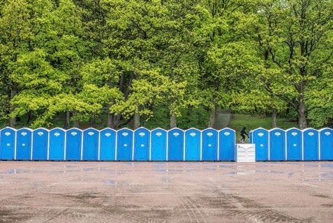 Long row of portable toilets in front of a forest where one has tipped over
