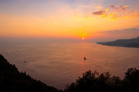 Looking down from Alanya Castle, the orange-red evening sun falls into the sea on the horizon of