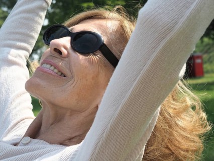 Joyful senior woman stretches in a lush park, smiling under the warm sun. She exudes contentment