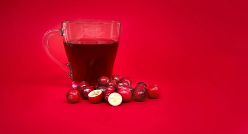 Red cranberries and transparent cup containing a dark red cranberry juice against a vibrant red