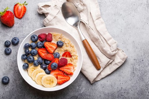 Oatmeal porridge with fruit and berries in bowl with spoon on white wooden background table top