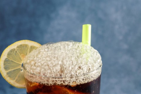 Cola with ice and lemon with foam spilling out of the crystal glass