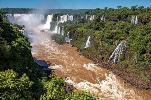 View of Iguazu Falls gorge and Devil's Throat with brown river, white cascading falls and lush