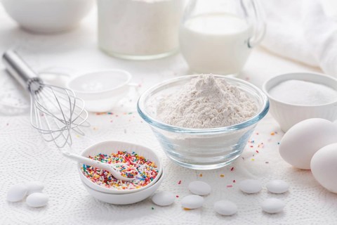 Baking background with flour, eggs, sugar sprinkles, kitchen tools, utensils in white