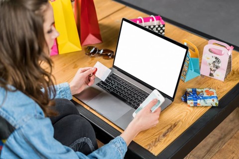 Young woman sitting front laptop with blank screen holding mobile phone credit card hand