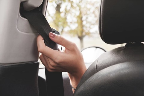 A woman's hand reaches behind her seat belt to fasten it. The concept of safe driving of women by