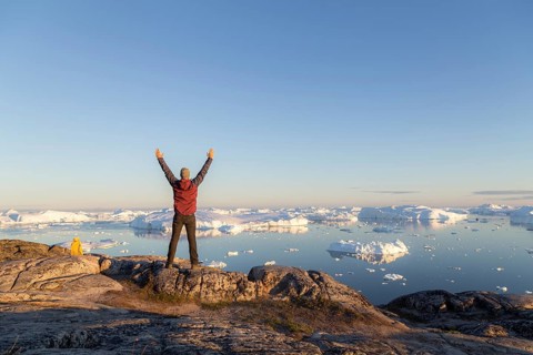 Ilulissat, Greenland, July 7, 2018: Young man looking at the Ilulissat Icefjord during midnight sun
