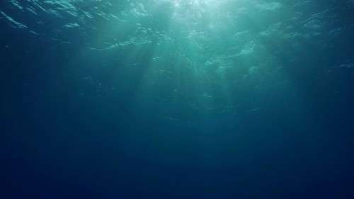 View of sun light from blue abyss, slow motion. Light filters down through blue water. Underwater