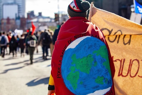 An environmental demonstrator is viewed from behind, marching on a crowded street with during a