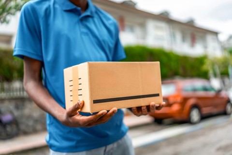 Close-up of a cardboard package on hands of a delivery man on blue uniform standing on street