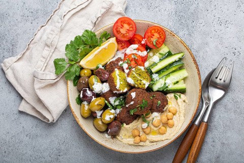 Falafel salad bowl with hummus, vegetables, olives, herbs and yogurt sauce. Vegan lunch plate top