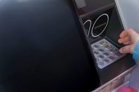 Woman typing her PIN number into an ATM machine to withdraw cash