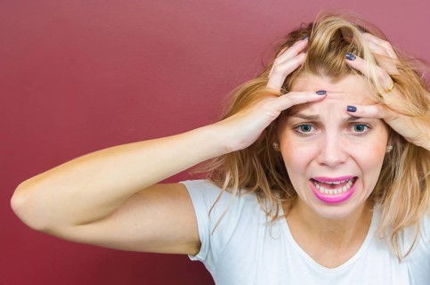 Concept of worry, woman with both hands on head on red background