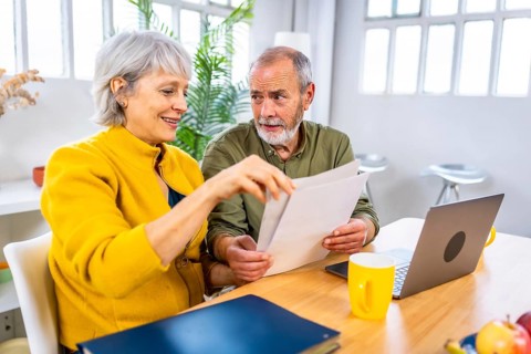Senior couple looking at financial bills using laptop together at home