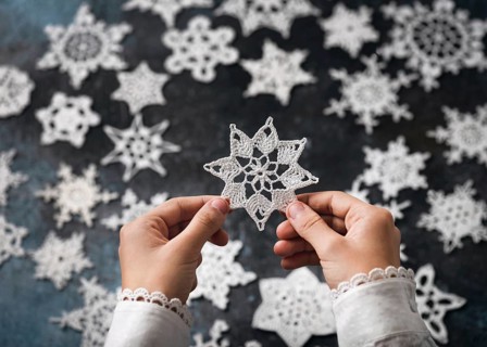 A crocheted snowflake, star made of white cotton in the girl's hands as a small handmade Christmas