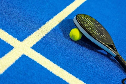Photo with no people and copy space of a paddle tennis racket leaning on ball in a blue court
