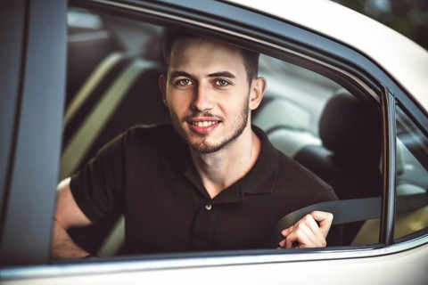 Young, handsome man fastens a seat belt, sitting in the back seat of the car