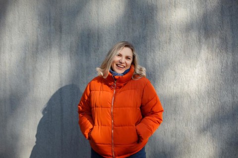 Happy positive middle-aged woman in orange down jacket smiling at camera while posing against