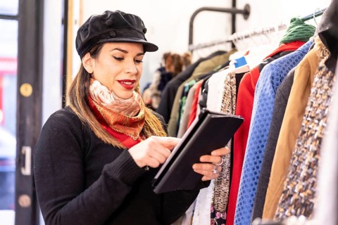 Latina clothing store clerk placing an order with a tablet, second-hand and sustainable clothing