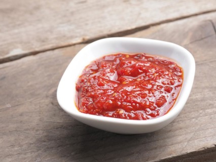 Very spicy chili sauce in a white bowl on a rustic wooden kitchen table, space for your text