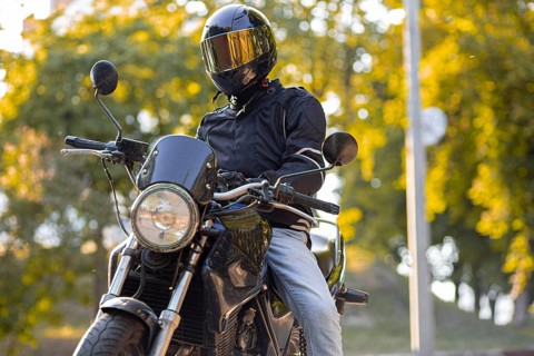 A motorcyclist wearing a helmet stands with a bike on a leafy street