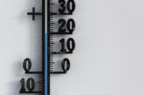 Classic black analog thermometer hanging on white wall displaying blue temperature scale of twenty,