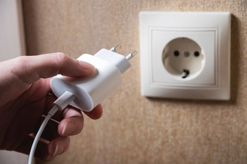 Hand turns on, turns off charger in electrical outlet on wall. White charger for phone in woman's