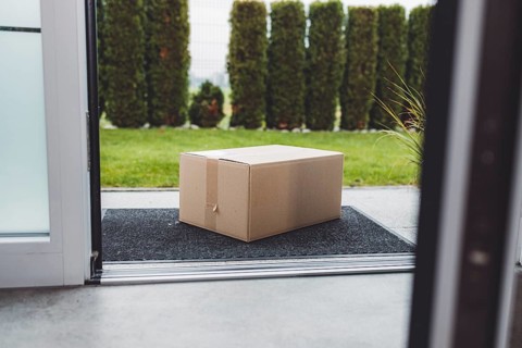 Delivery package, a cardboard box sitting in front of the front door, waiting to be picked up.