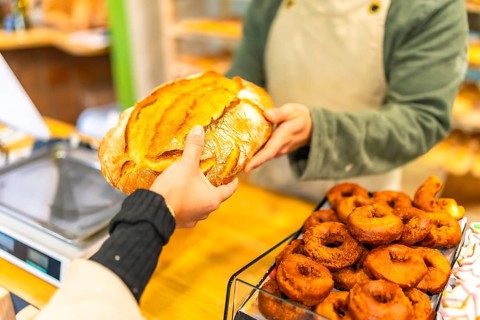 Close-up of the hands of a salesman handing a round artisan bread to a female customer