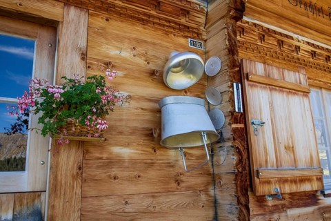 A rustic wooden wall with a window, a flower box and a decorative milk churn, typical alpine