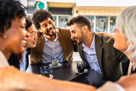 Multi-ethnic business team congratulating and celebrating embracing together sitting in a cafeteria