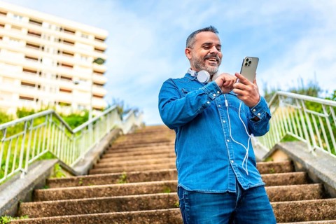 Low angle view photo of a mature man using phone and headphones standing on city stairs