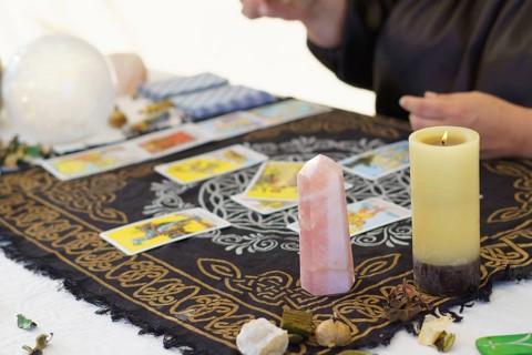 Hands of an unrecognizable fortune-teller woman dressed in black sitting at her table reading tarot