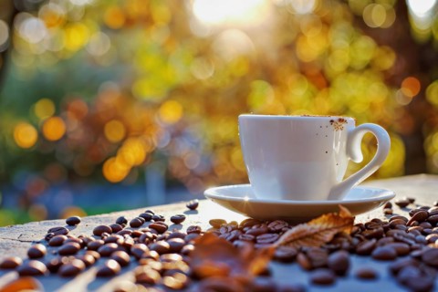 A coffee cup surrounded by coffee beans and autumn leaves with warm bokeh lighting effects in the
