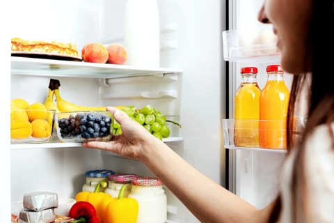 Woman hand taking, grabbing or picks up box of blueberry out of open refrigerator shelf or fridge