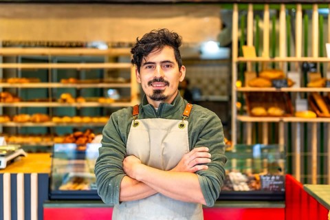 Formal portrait of a latin male young baker standing proud with arms crossed in a modern artisan