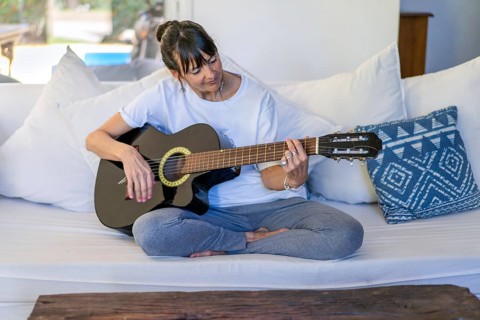 Adult woman playing the guitar while seated on her sofa at home