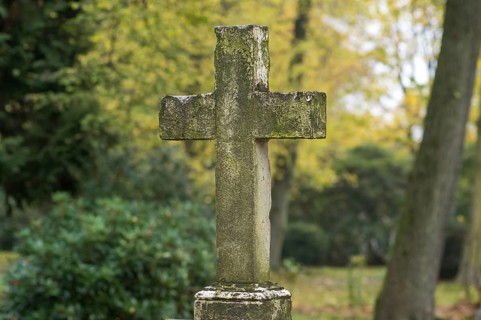 Weathered stone cross tombstone in a cemetery during the fall season