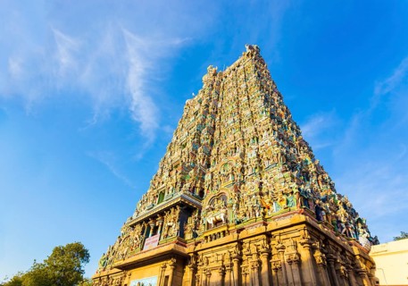 West tower gateway of Meenakshi Amman Temple covered in colorful statues of gods on a blue sky day