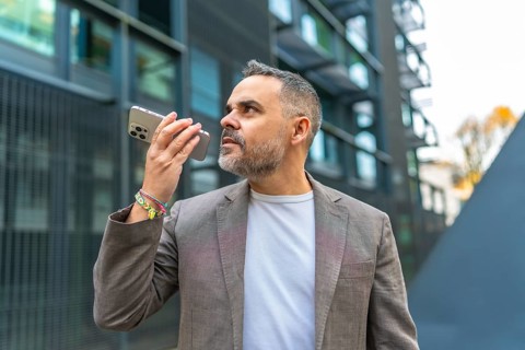 Mature male caucasian businessman sending a voice message in the street next to a financial