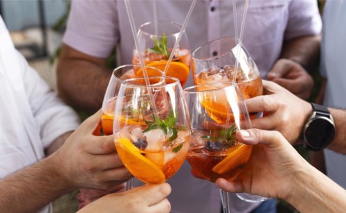 Happy friends spending time together, focus on young women drinking Aperol spritz cocktail. Summer
