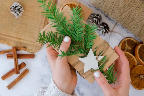 Woman making Box with New Year's gifts, wrapped in craft paper and decorated with fir branch.