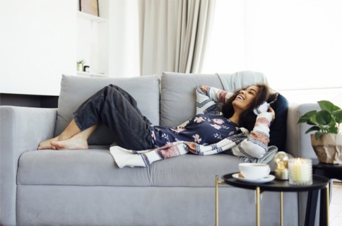 African millennial woman wearing white wireless headphones, listening music, resting and lying on