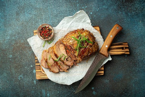 Rolled turkey roasted with spices and herbs on baking paper with knife and rustic concrete